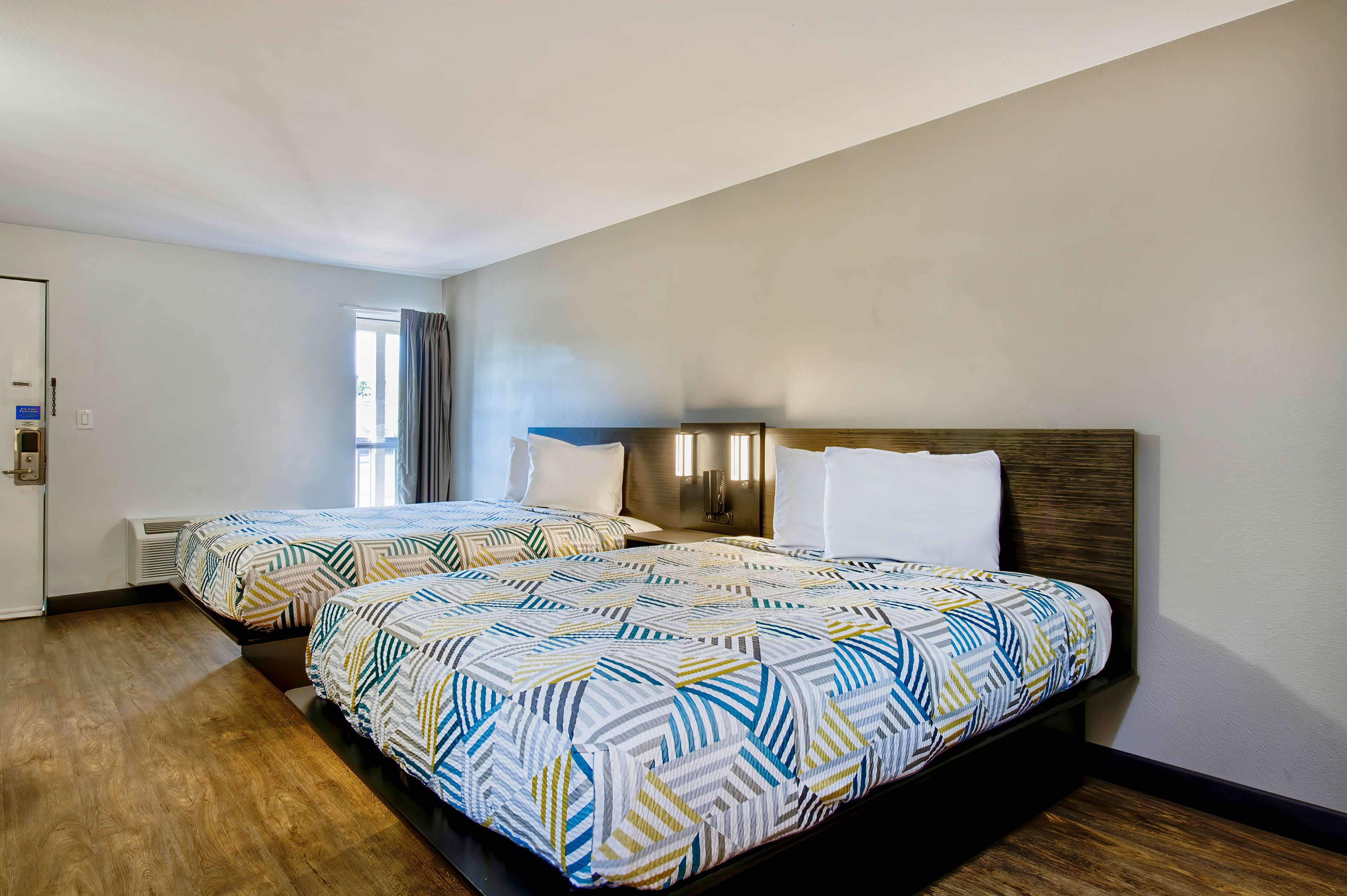 A hotel room with two beds, each with patterned bedding, a wooden headboard, and a window with curtains.