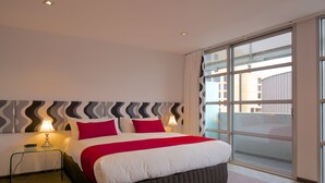 A modern hotel room with a large bed, two bedside lamps, and a view of the city through large windows. - Zero Davey Boutique Hotel (Hobart)