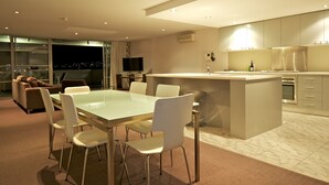 A modern kitchen with a central island, a dining area with a glass table, and a sofa in the background. - Zero Davey Boutique Hotel (Hobart)