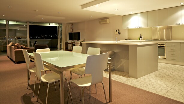 Una cocina moderna con una isla central, un comedor con mesa de vidrio y un sofá al fondo.