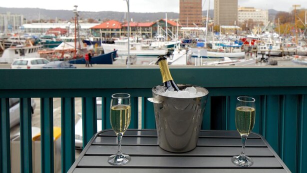 A balcony with a view of a marina, a champagne bottle in an ice bucket, and two glasses of champagne. - Zero Davey Boutique Hotel (Hobart)