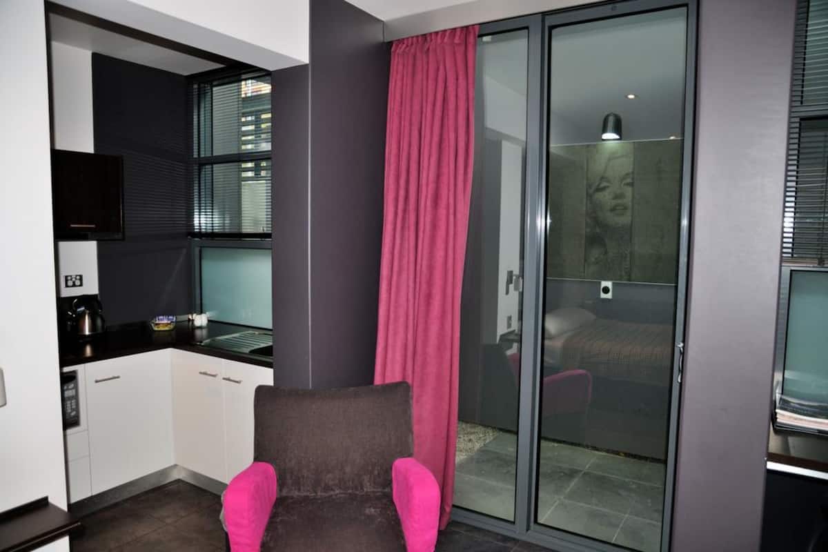 A compact room with a kitchenette, a sliding glass door leading to a bedroom, and a pink chair.
