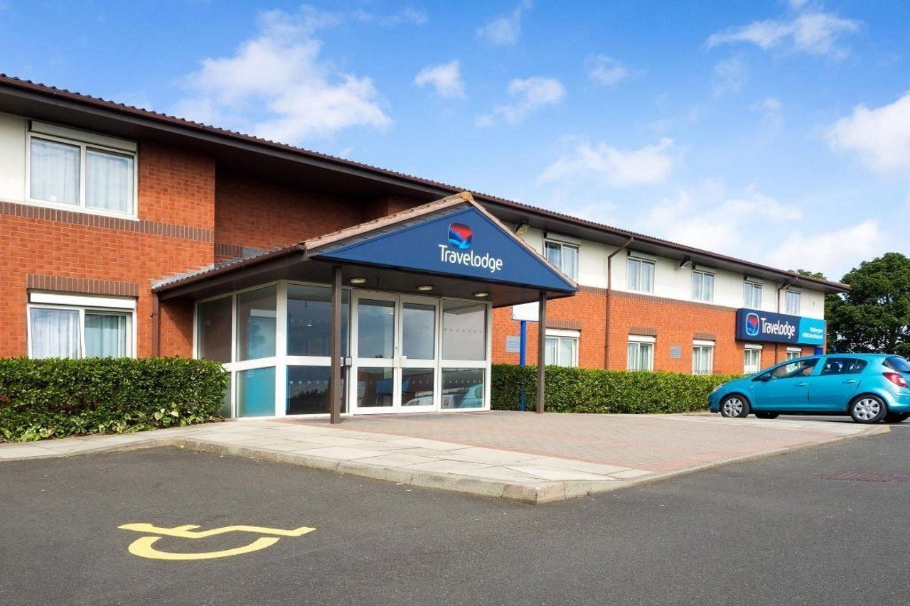 Un hôtel Travelodge avec une entrée bien visible, un espace de stationnement et une voiture bleue garée à l’extérieur.