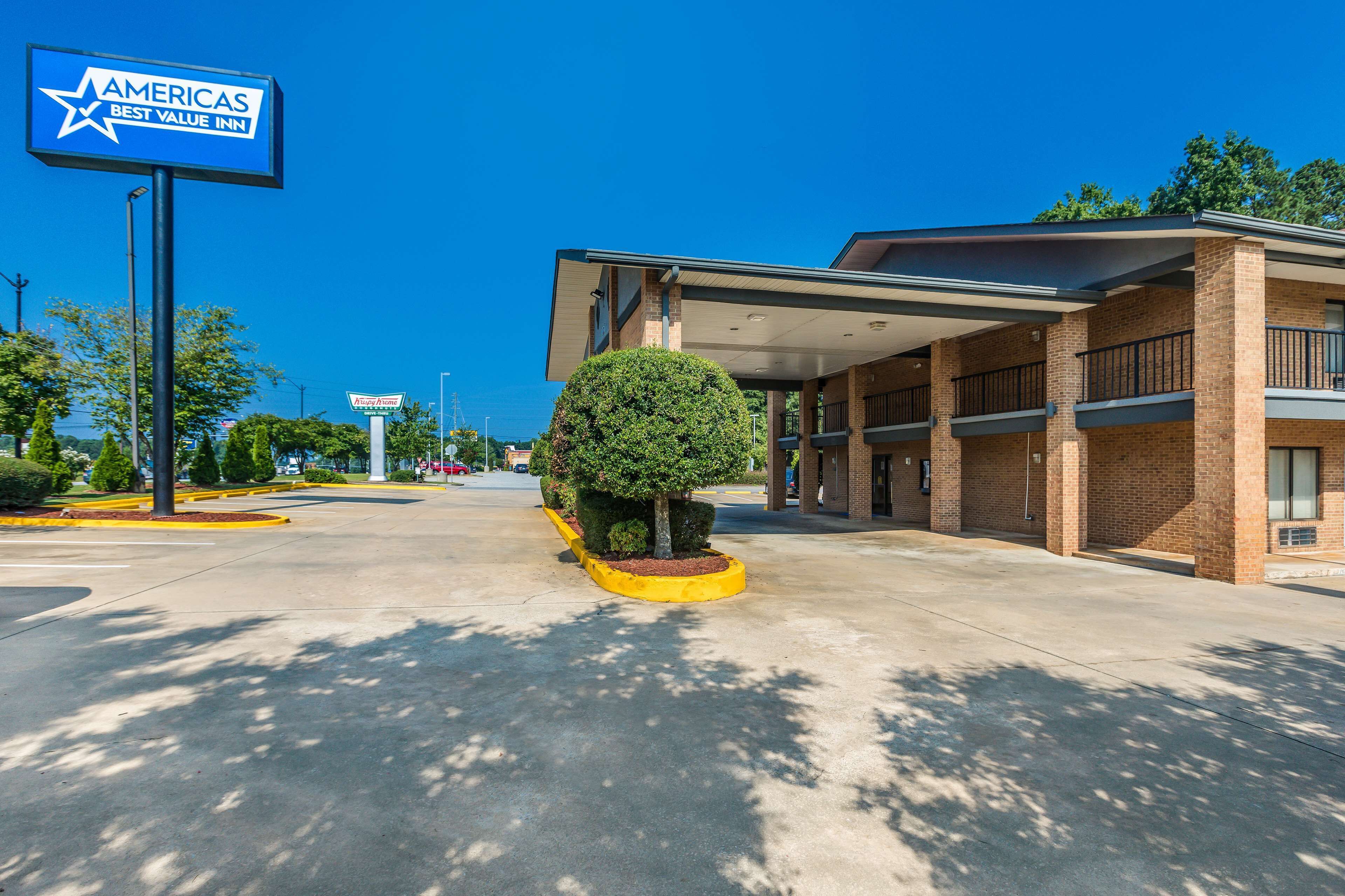 Un hotel moderno con estacionamiento techado, un letrero llamativo del Americas Best Value Inn y un área ajardinada bien cuidada con arbustos podados.