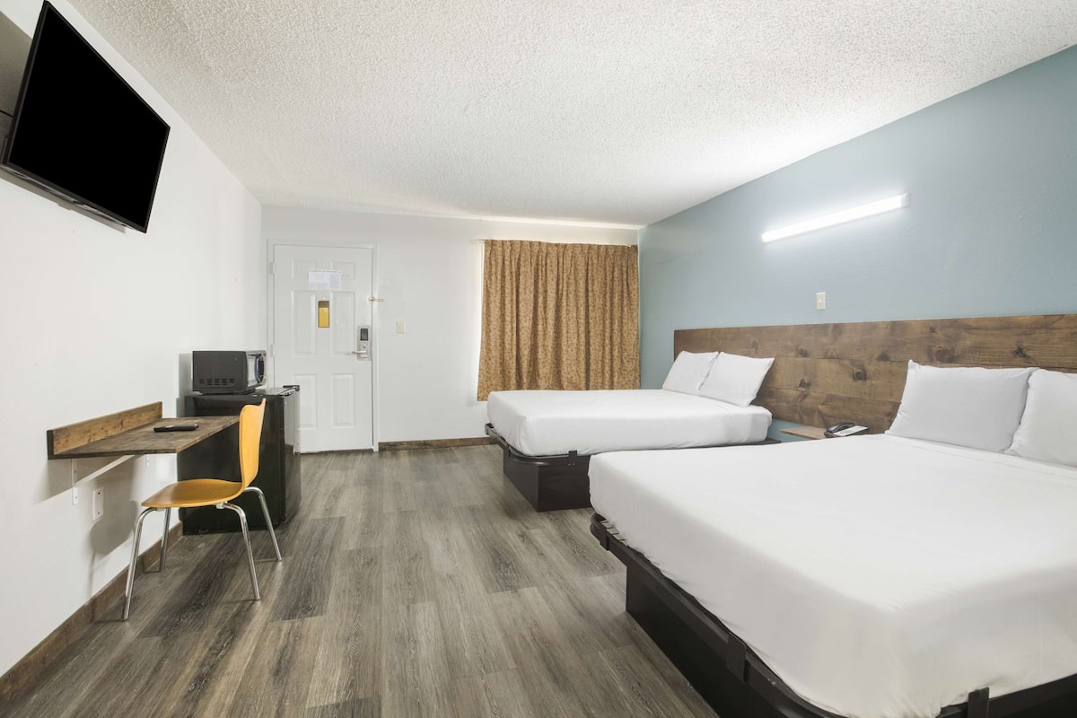 A hotel room with two beds, a desk with a chair, a television, and a door.
