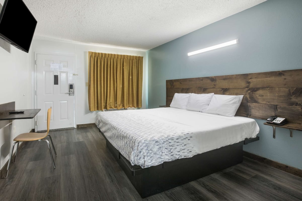 A hotel room with a bed, a desk, a chair, a television, and a window with curtains.
