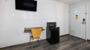 Habitació amb televisió de pantalla plana penjada a la paret, microones damunt un moble negre, una panxa de fusta i una porta amb una cerradura i un ull.