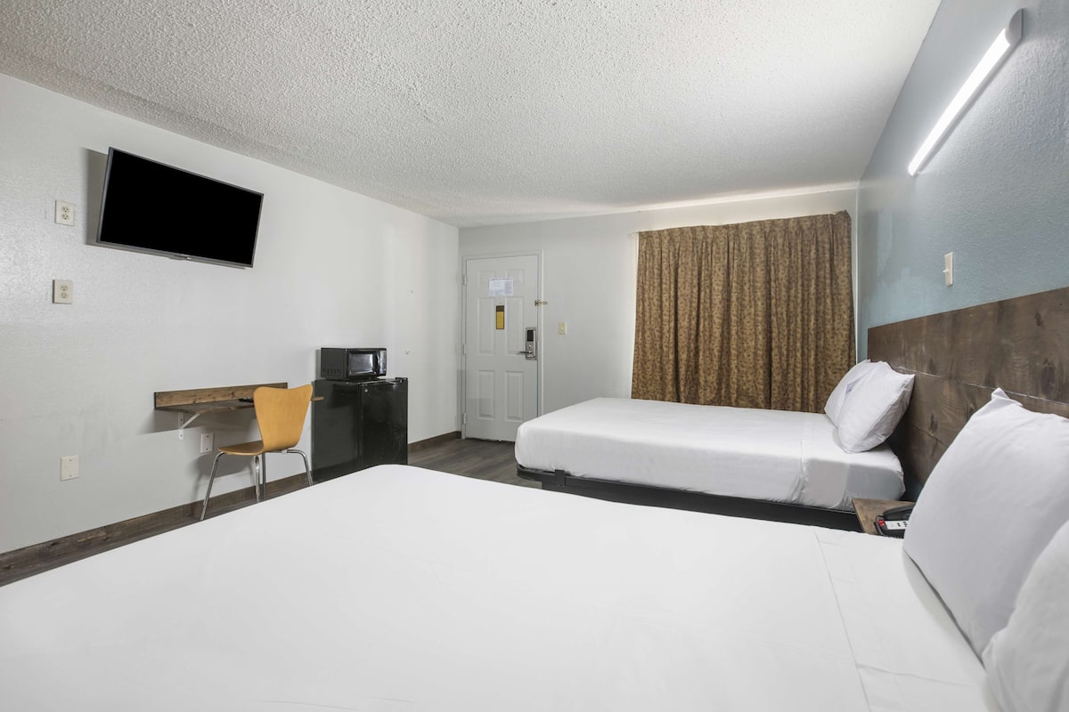 A hotel room with two beds, a desk with a chair, a television mounted on the wall, and a door.