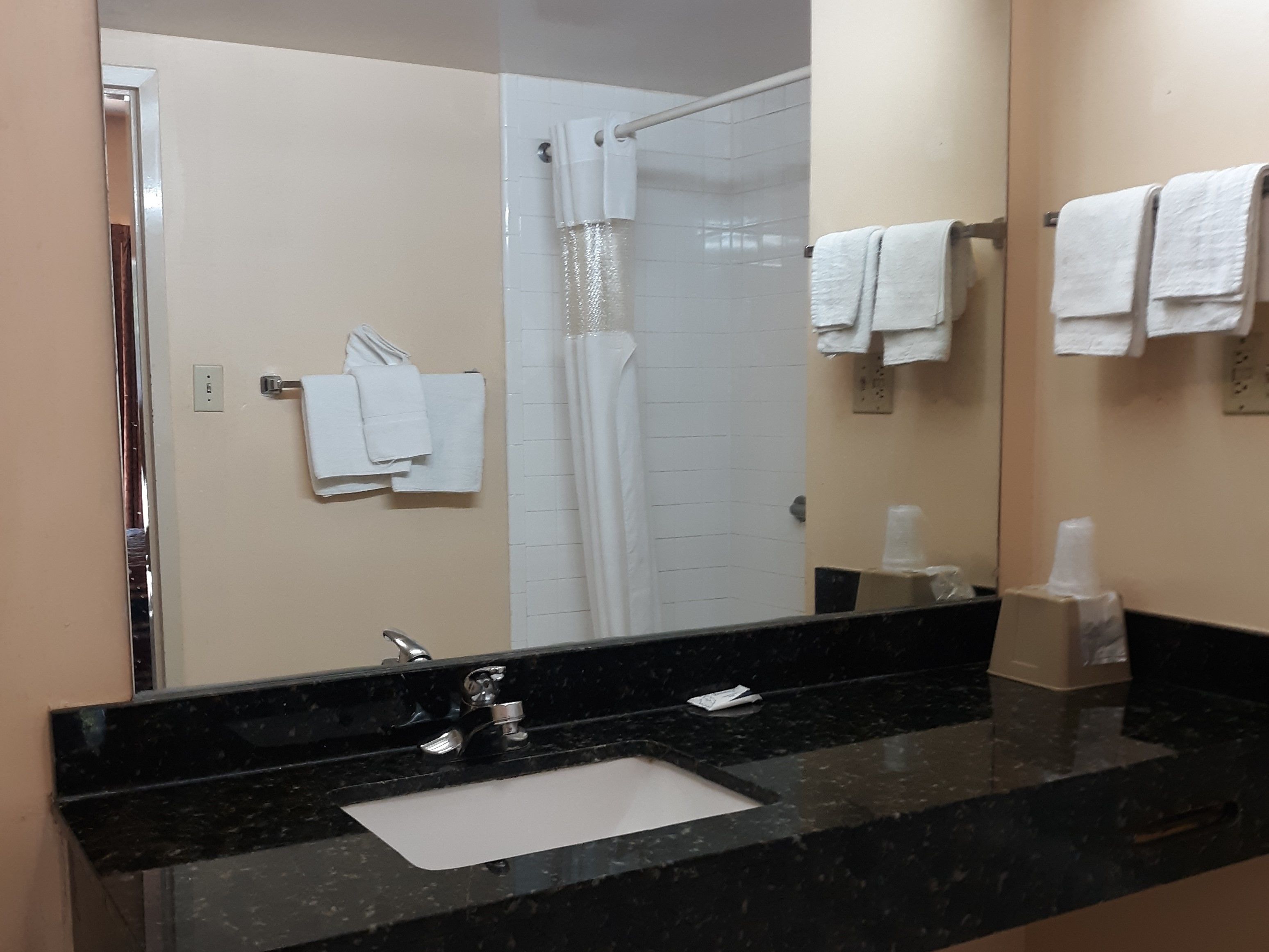 Une salle de bain avec un lavabo en marbre noir, des serviettes blanches, un rideau de douche et un miroir qui reflète la pièce.