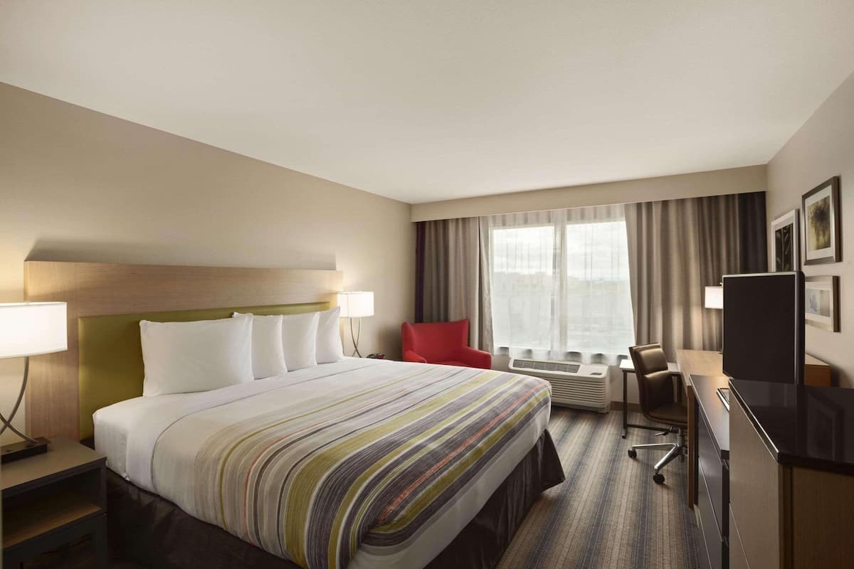 A hotel room with a large bed, a desk, a chair, a TV, and a window with curtains.