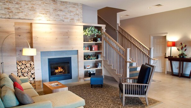 A living room with a fireplace, a staircase, and a bookshelf. - Country Inn & Suites by Radisson, Lewisburg, PA (Lewisburg)