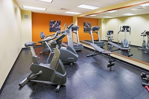 A gym with various cardio machines, a mirrored wall, and a black rubber floor.
