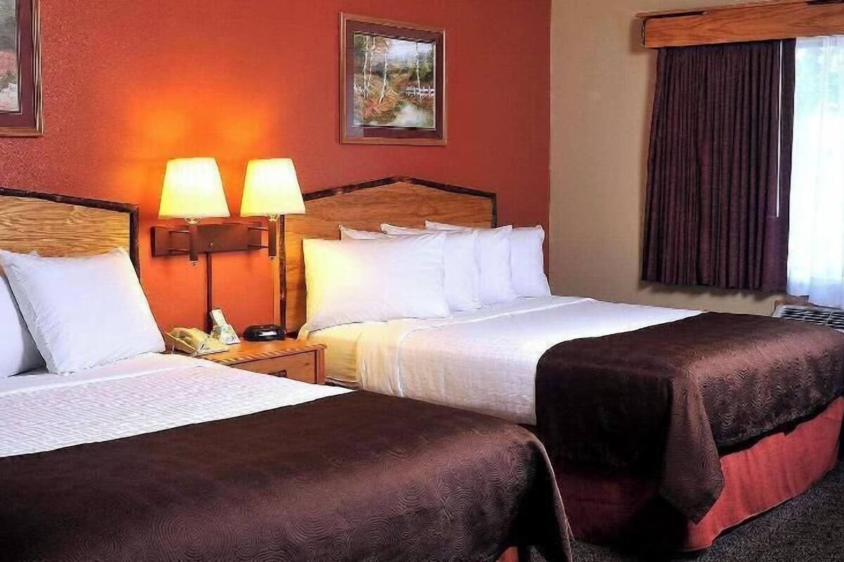 Ein Hotelzimmer mit zwei Betten, einem Nachttisch mit Lampen und einem Fenster mit Vorhängen.