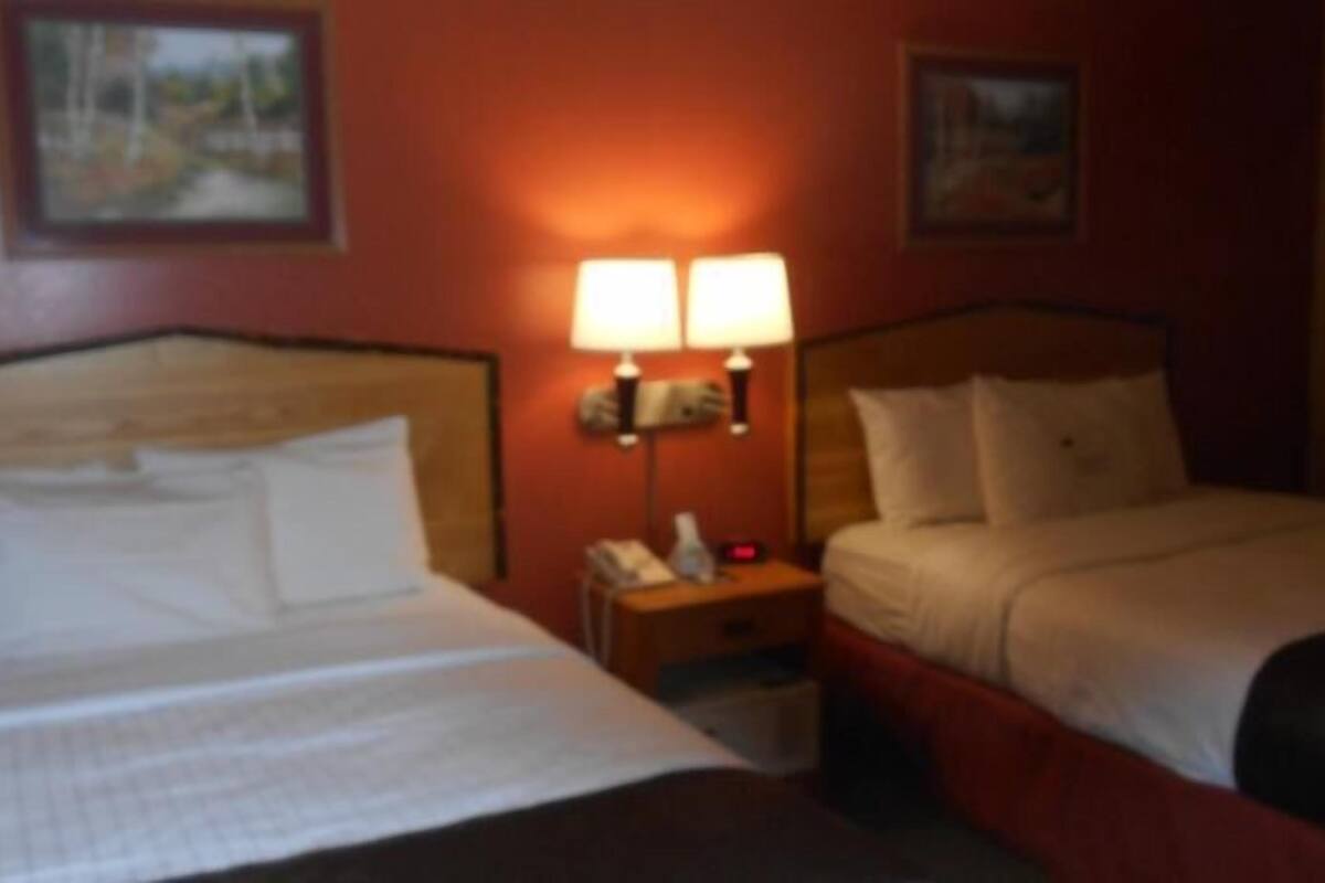 Ein Hotelzimmer mit einem großen Bett, einem Nachttisch mit einer Lampe und zwei gerahmten Bildern an der Wand.