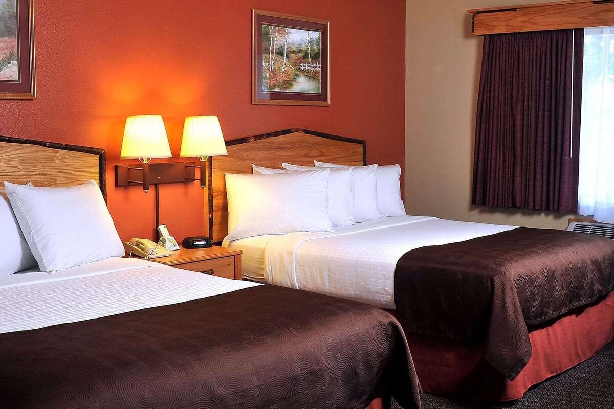 A hotel room with two beds, a wooden headboard, a nightstand with a phone, and two wall-mounted lamps.