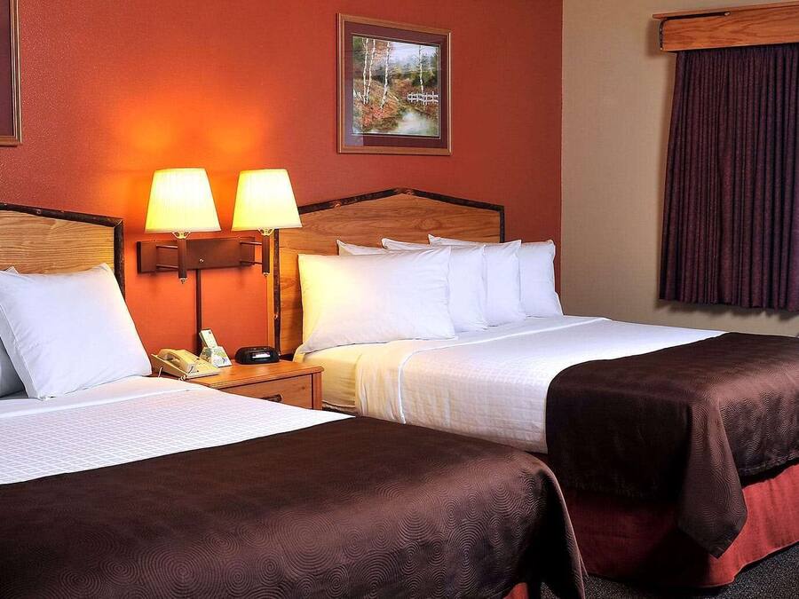 Habitación de hotel con dos camas, cabecero de madera, mesita de noche con teléfono y dos lámparas de pared.