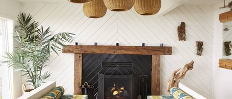 Una sala acogedora con chimenea, lámparas colgantes de mimbre y sofás estampados.