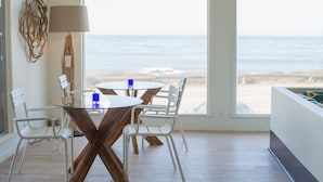 A dining area with a glass table and white chairs, a lamp, and a view of the beach. - Cambria Beach Lodge (Cambria)