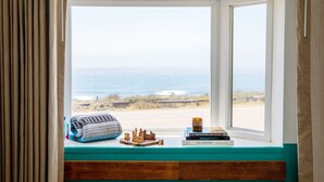 A window with a view of the beach and ocean, a chessboard, a book titled "The Chopper," and a rolled-up towel on a wooden ledge. - Cambria Beach Lodge (Cambria)