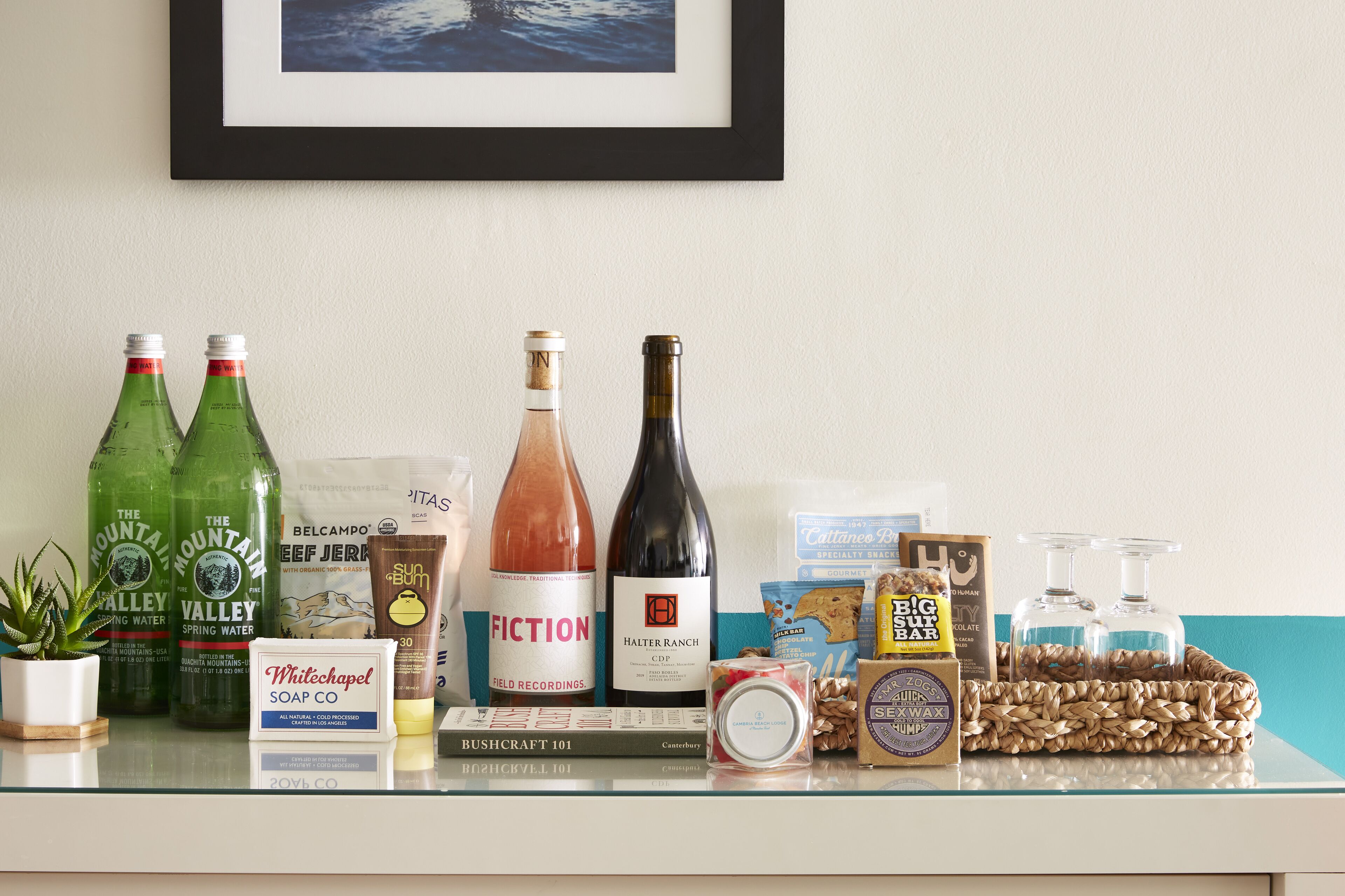 A shelf with various items including bottles of water, a bottle of wine, a book, and some toiletries.