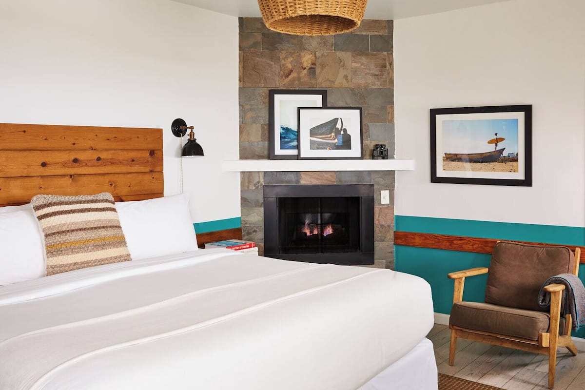 Quarto com cama grande, cabeceira de madeira, lareira e uma cadeira.