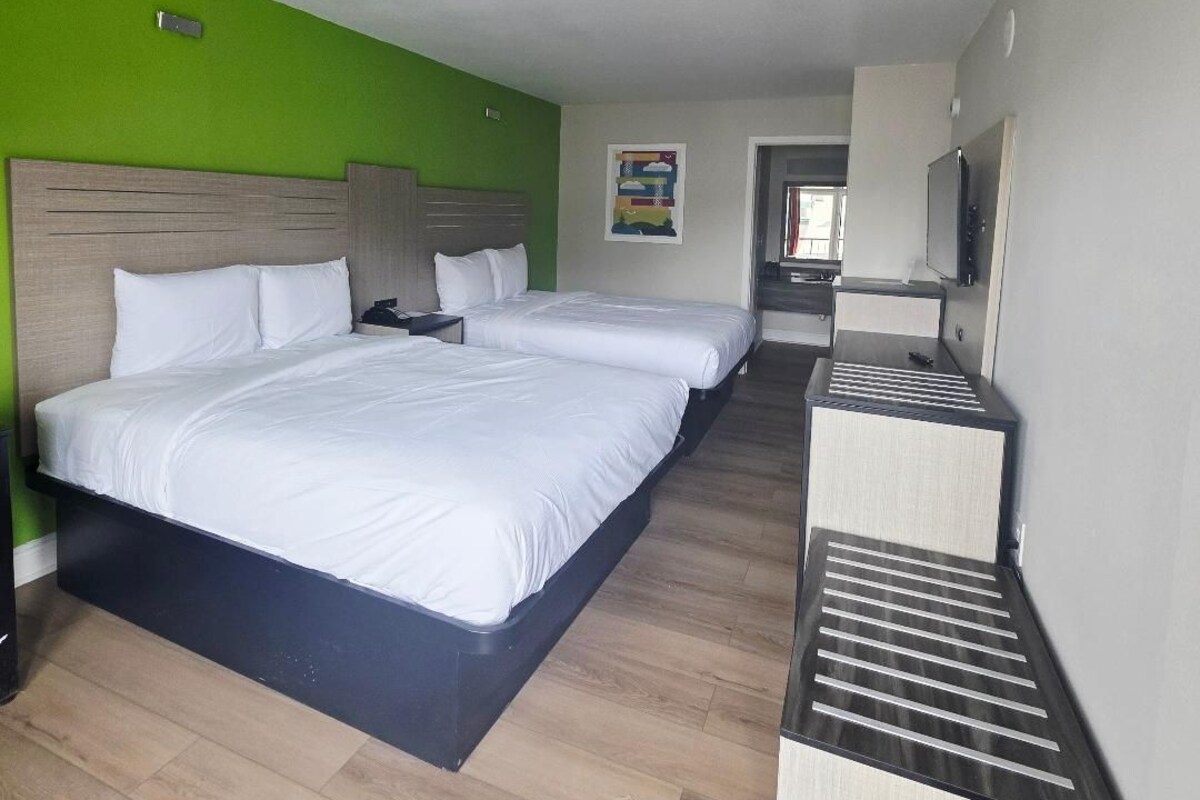 Habitación de hotel con dos camas, un escritorio pequeño, un cesto de basura y un televisor.