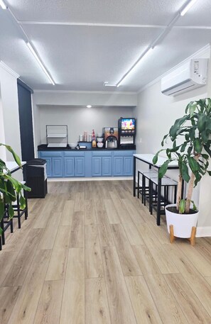 A modern kitchen with blue cabinets, a wooden floor, a coffee machine, and a TV.