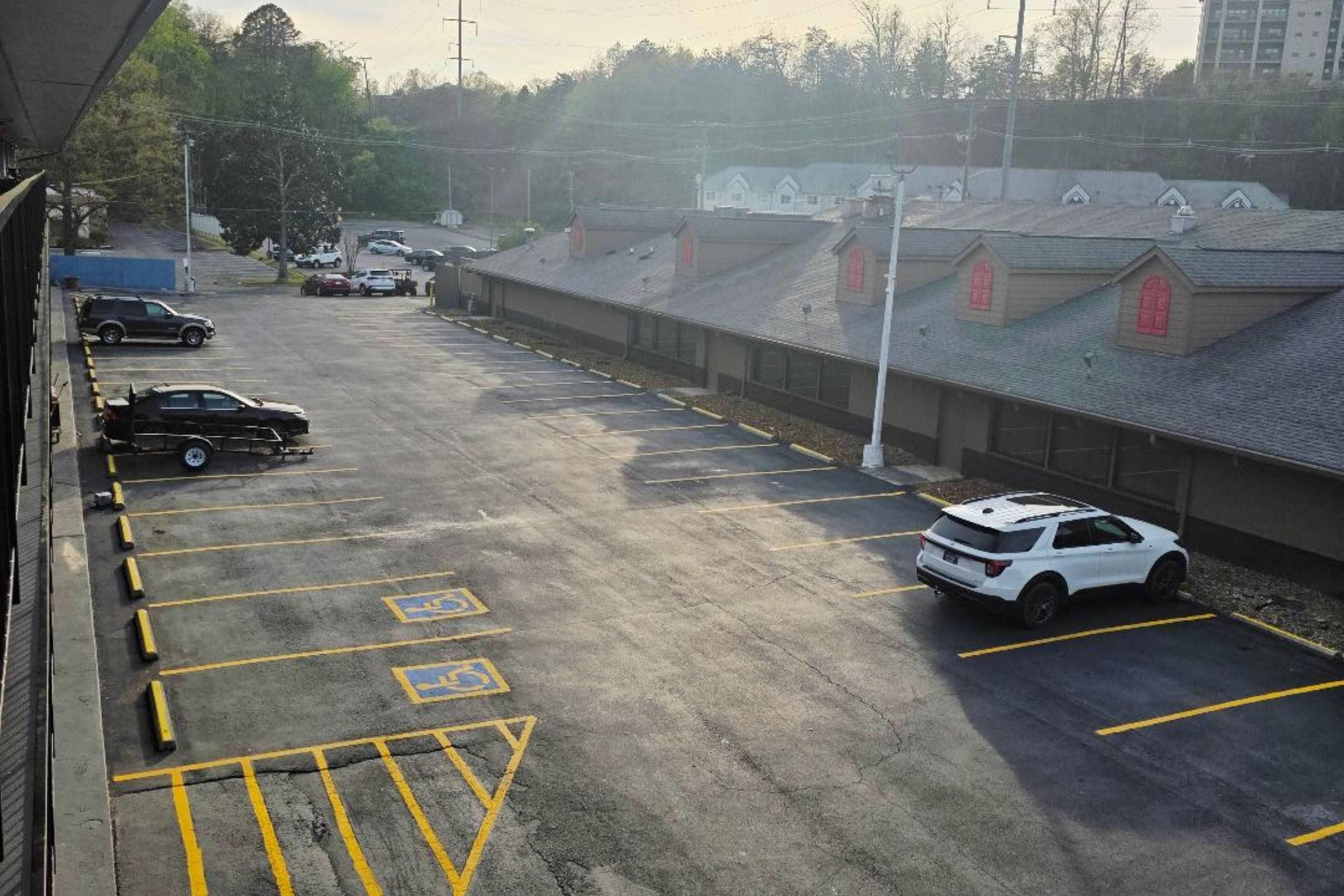 A parking lot with multiple cars, marked parking spaces, and a building with a sloped roof in the background.