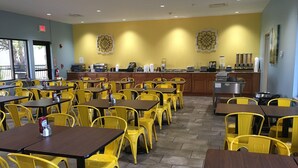 Un restaurant avec des chaises et des tables jaunes, un espace cuisine et un mur bleu agrémenté d’éléments décoratifs.