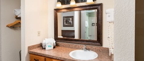 Un baño con tocador de madera, lavamanos blanco y un espejo grande con marco decorativo.