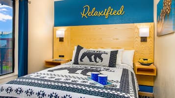 A hotel room with a bed, a headboard with a 'Relaxified' sign, two bedside lamps, a nightstand with a lamp, a window with curtains, and a painting on the wall.