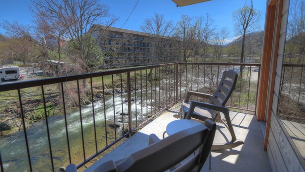 Un balcon donnant sur une rivière, une chaise et un bâtiment en arrière-plan.