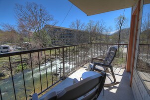 A balcony with a view of a river, a chair, and a building in the background.
