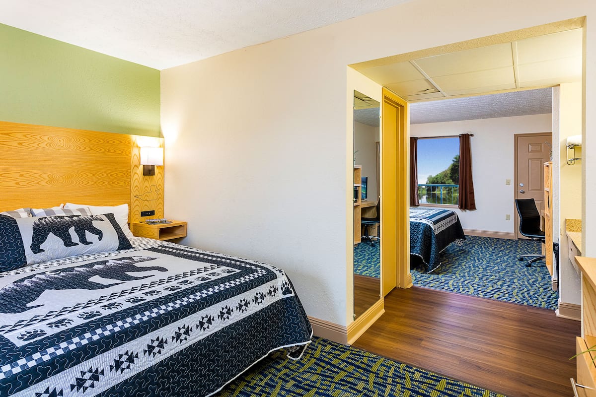 A hotel room with a bed, a desk, a chair, and a view through an open door.