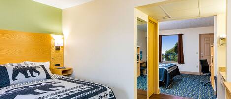 Habitación de hotel con cama, escritorio, silla y vista por una puerta abierta.