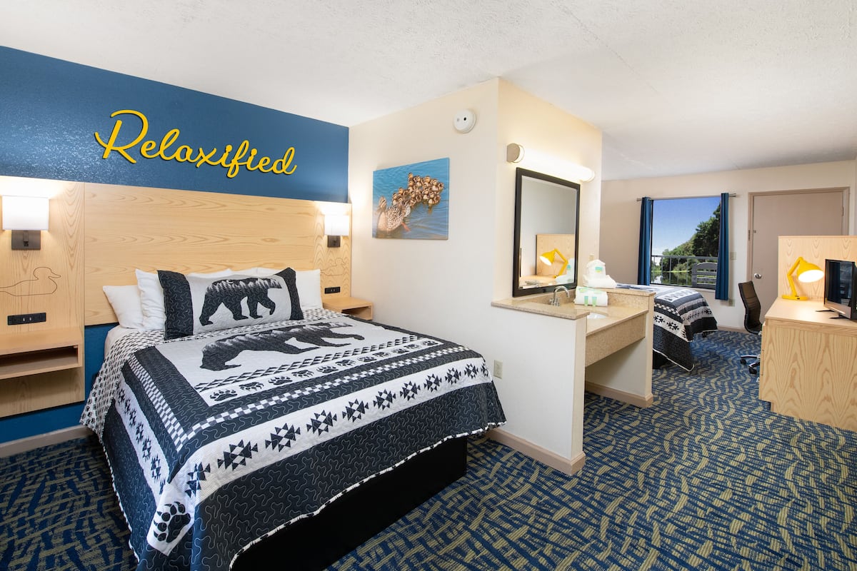 A hotel room with a bed, a desk, a mirror, and a window.