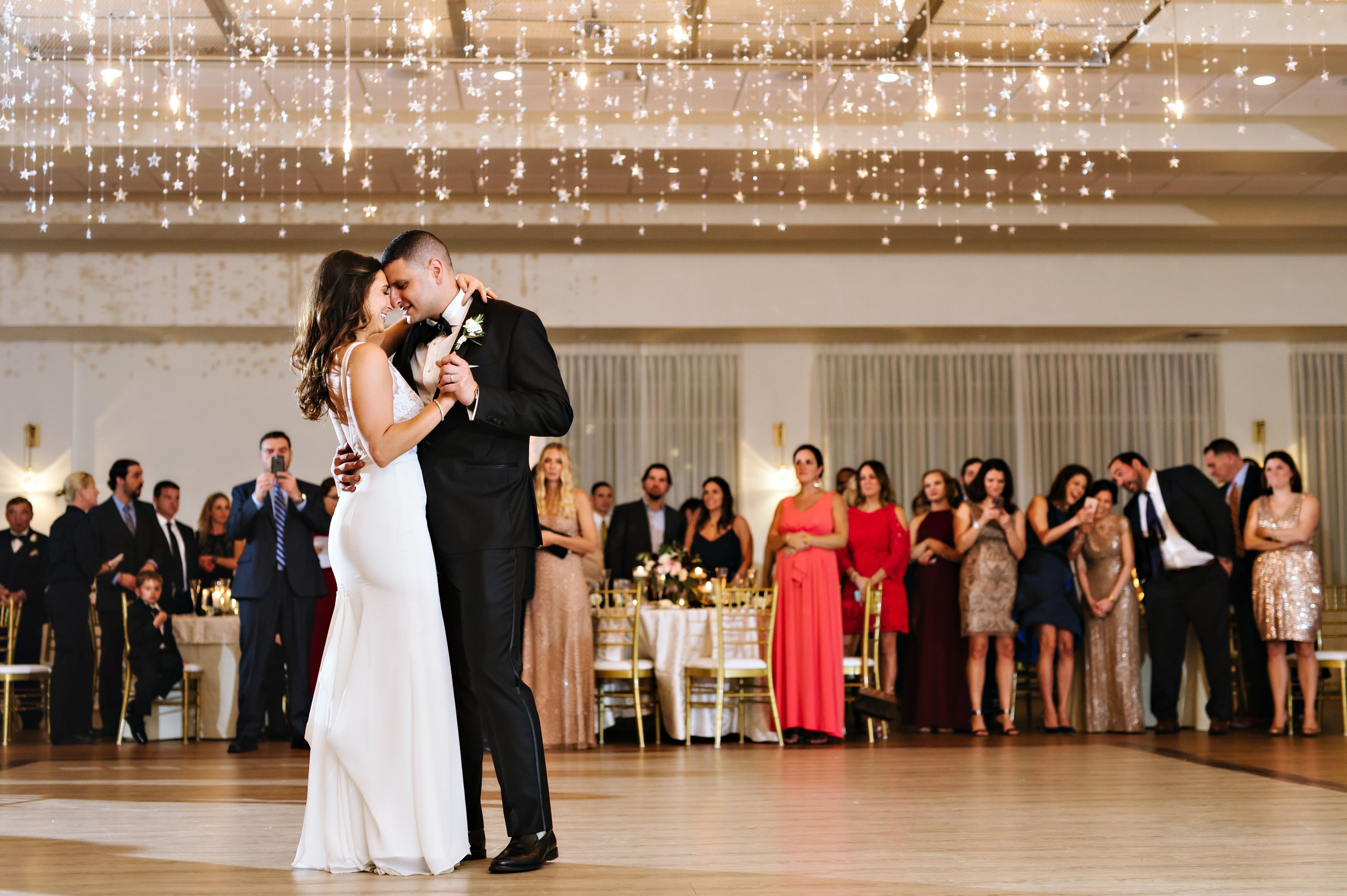 A wedding reception with guests seated at tables, a dance floor, and string lights overhead.