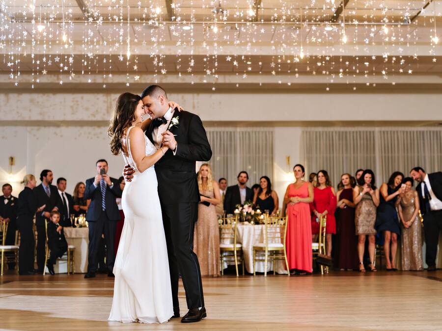Uma receção de casamento com convidados sentados a mesas, uma pista de dança e luzes de corda no teto.