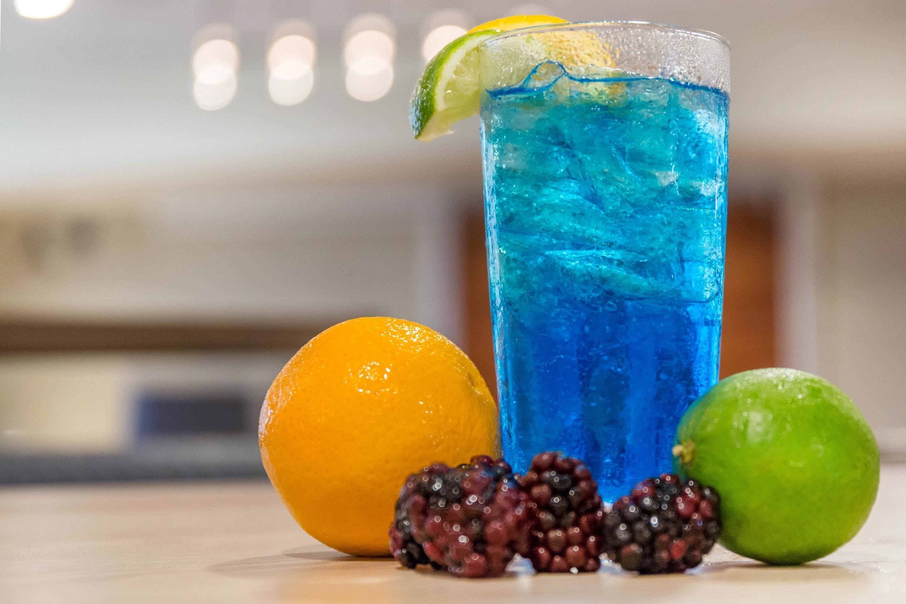 Un bicchiere di bevanda blu con una fetta di lime, un'arancia, more e un altro lime su un tavolo.