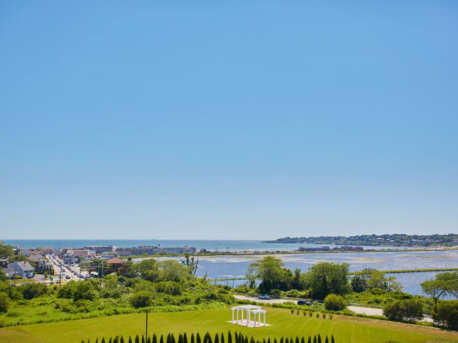 A coastal town with a clear view of the sea, a grassy area with a gazebo, and buildings along the waterfront.
