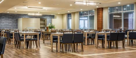 Un vaste espace dédié à la salle à manger, avec de nombreuses tables et chaises, de grandes fenêtres et un design moderne au niveau du plafond.