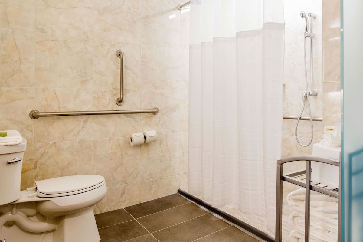 Une salle de bain équipée de toilettes, d’une barre d’appui, d’une douche avec une porte en verre et d’un porte-serviettes.