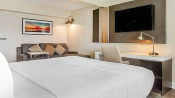 A hotel room with a large bed, a desk with a chair, a television mounted on the wall, and a painting on the wall.