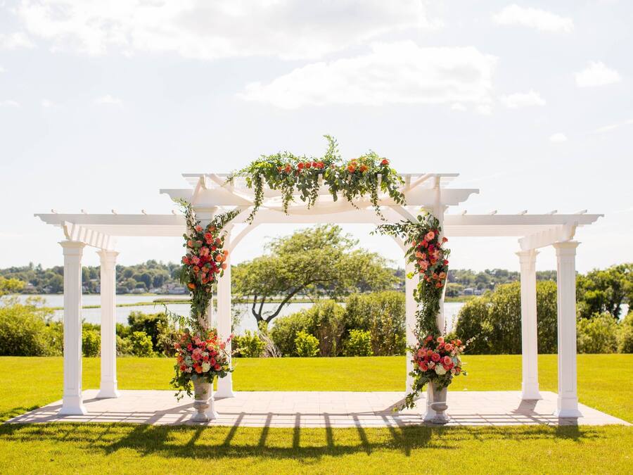 Een witte pergola met bloemversiering en uitzicht op een meer.