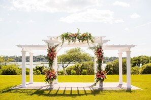 A white pergola with floral decorations and a view of a lake.