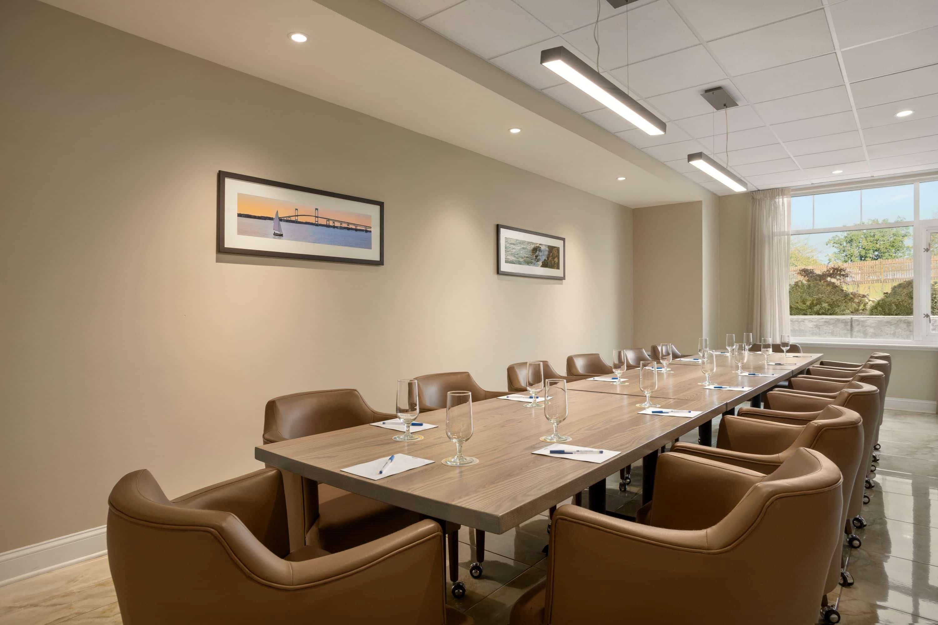 A conference room with a long table, brown leather chairs, and framed pictures on the walls.