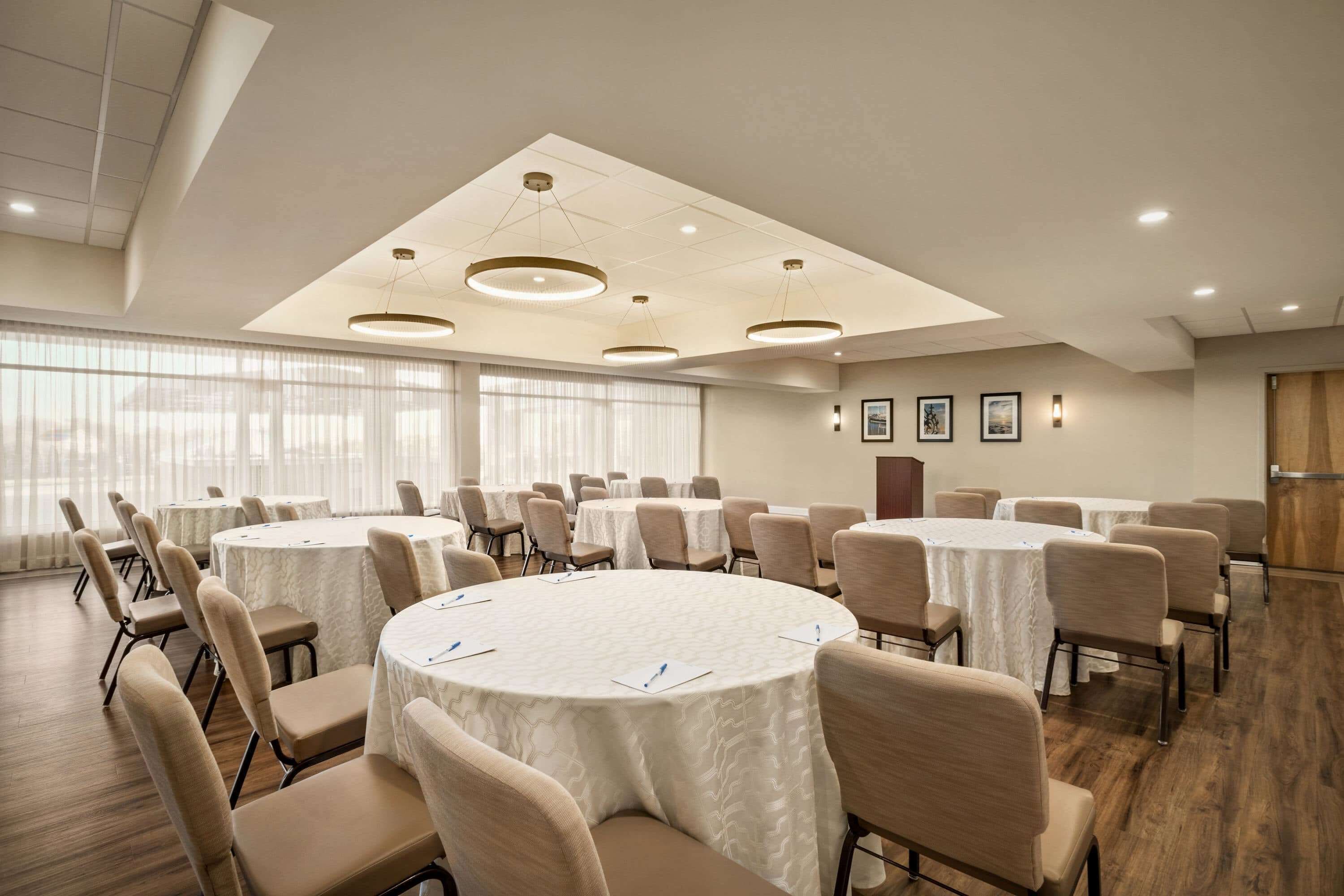 A conference room with multiple round tables, beige chairs, and a modern ceiling design.