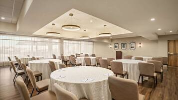 A conference room with multiple round tables, beige chairs, and a modern ceiling design.