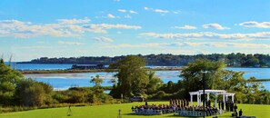 A wedding ceremony outdoors with a view of a lake and distant buildings.