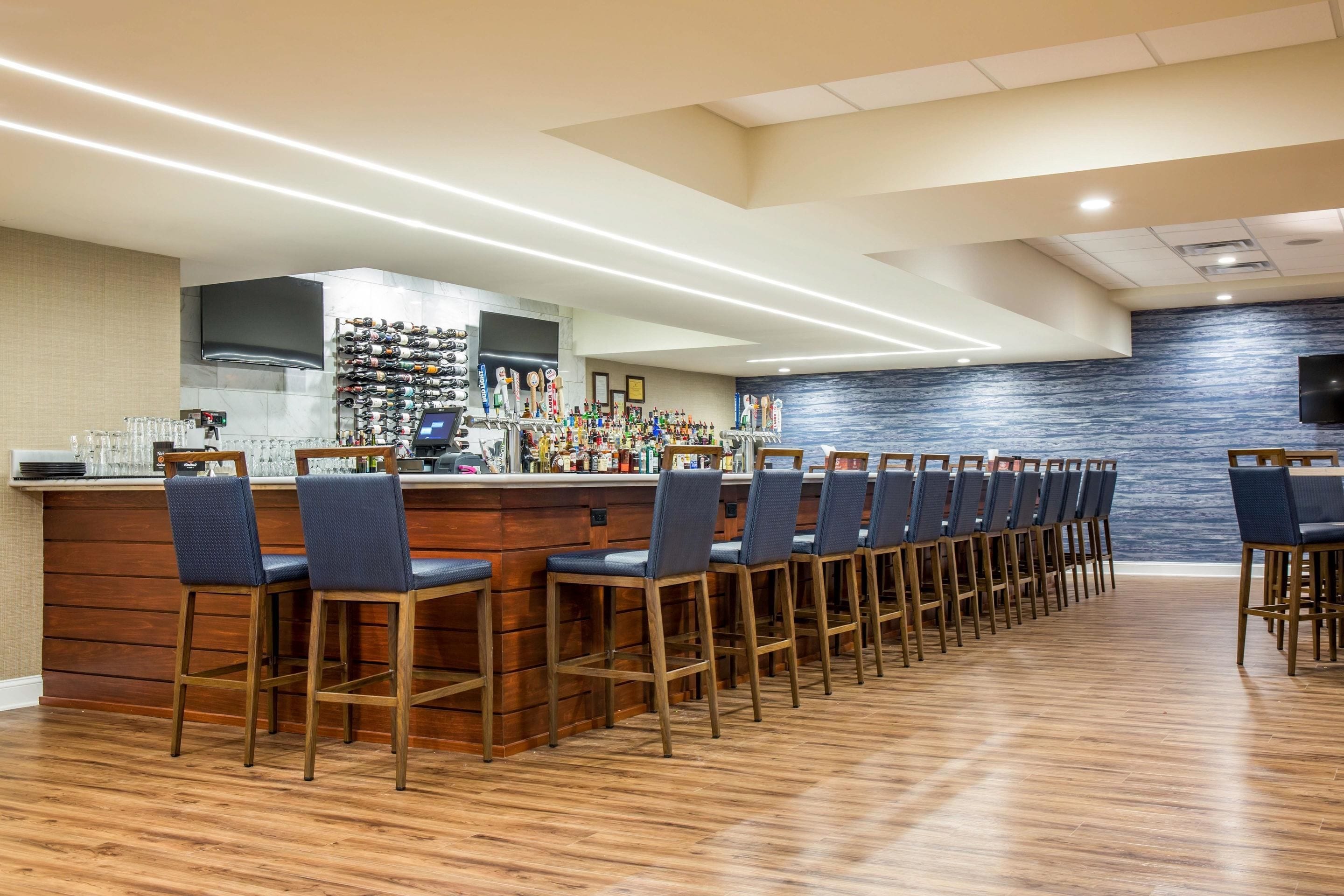 A bar area with a long counter, multiple bar stools, and a wall of liquor bottles.